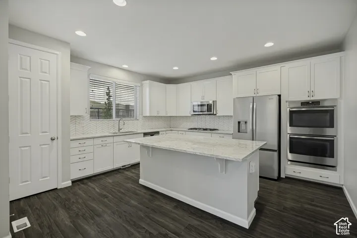 White shaker cabinetry with stainless steel appliances, a center island, and wood-finish flooring