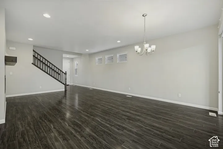 Spacious interior featuring wood-finish flooring, a dark-stained staircase with white risers, multiple recessed ceiling lights, and a five-light chandelier