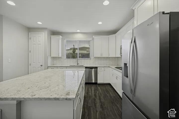 Spacious kitchen featuring an expansive island, white cabinetry, a herringbone tile backsplash, stainless steel appliances, and wood-finish flooring