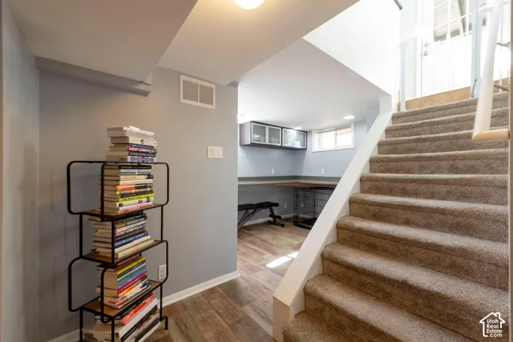 Carpeted staircase with white railing, wood-finish flooring, built-in desk, and wall-mounted cabinetry