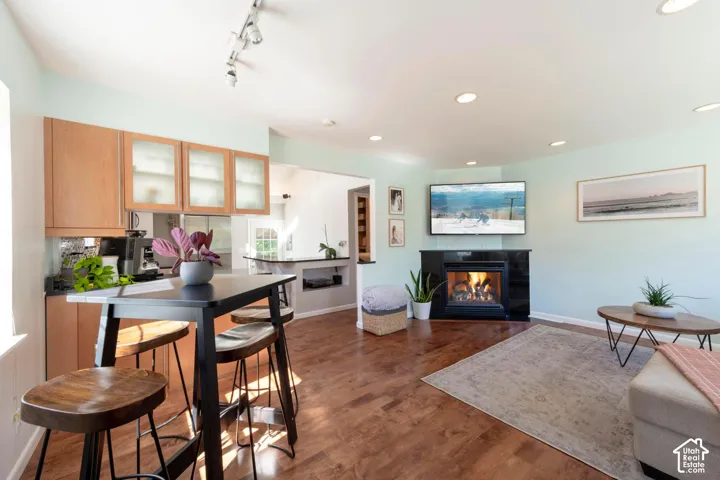 Hardwood flooring, corner-mounted fireplace with black surround, recessed lighting, track lighting, and wood cabinetry with frosted glass inserts