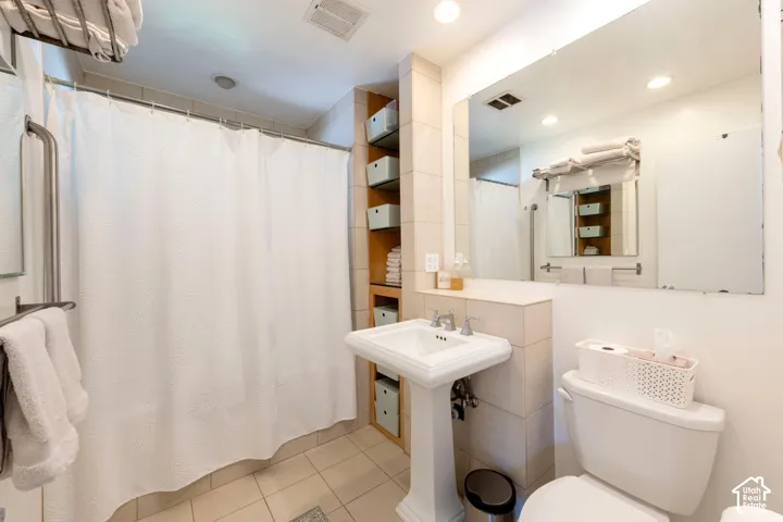 Pedestal sink, recessed shelving, tile flooring, full-width mirror, and overhead lighting