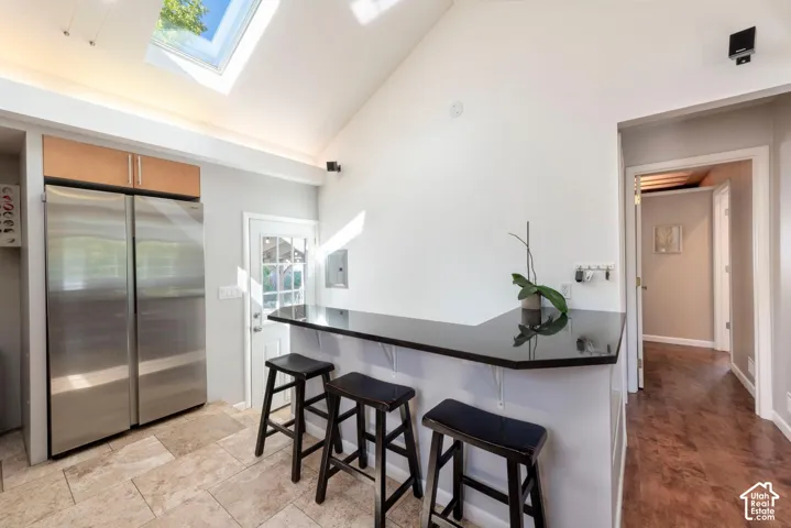 Vaulted ceilings with skylight, stainless steel side-by-side refrigerator, wood-finish upper cabinetry, black countertop, and tile flooring