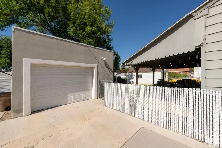 Attached garage with a panel garage door, paved driveway, stucco exterior, and a chain-link fence