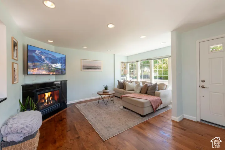 Living area featuring hardwood flooring, a corner fireplace with a black tile surround, recessed lighting, and a bay window