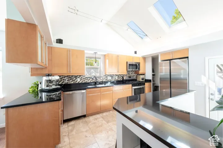 Vaulted ceiling with skylights, stainless steel appliances, black countertops, wood-finish cabinetry, and tiled flooring