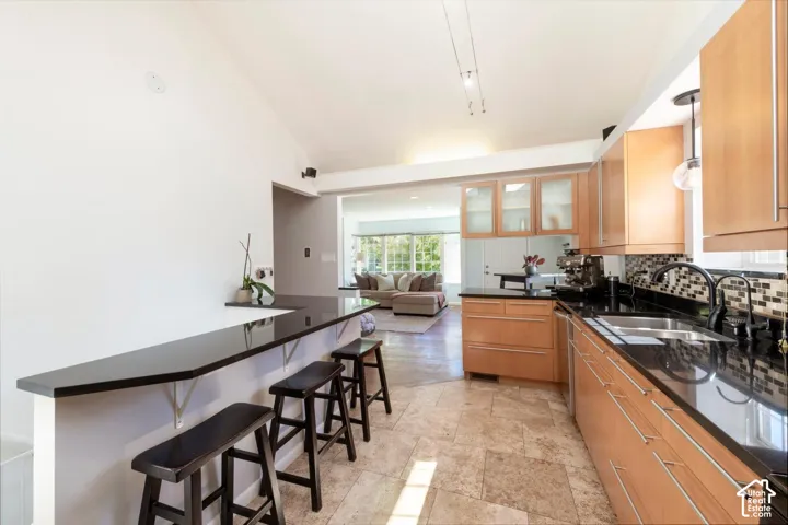 Kitchen featuring a breakfast bar, light wood-finish cabinetry, dark countertops, tile backsplash, and tile flooring