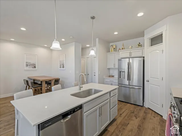 Spacious kitchen featuring an expansive island with a stainless steel sink, wood-finish flooring, light gray cabinetry, and stainless steel appliances