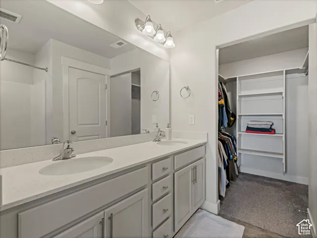 Primary Bath with walk in closet, Double vanity with a large mirror, chrome fixtures, and light-toned quartz  countertops