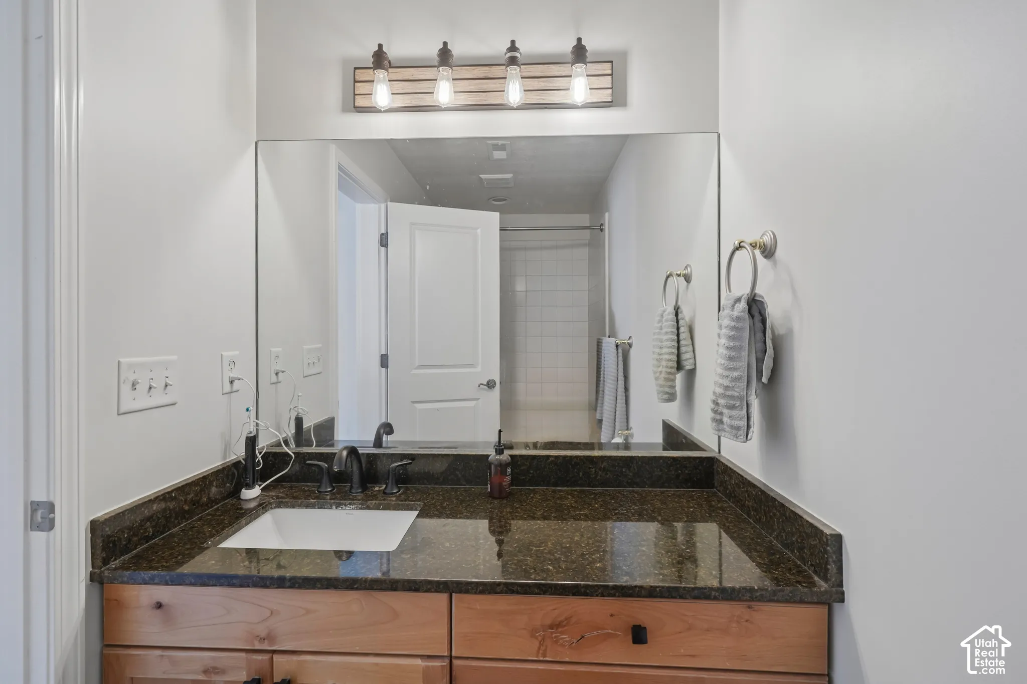 Vanity featuring a rectangular undermount sink, dark stone countertop, and light wood-finish cabinetry