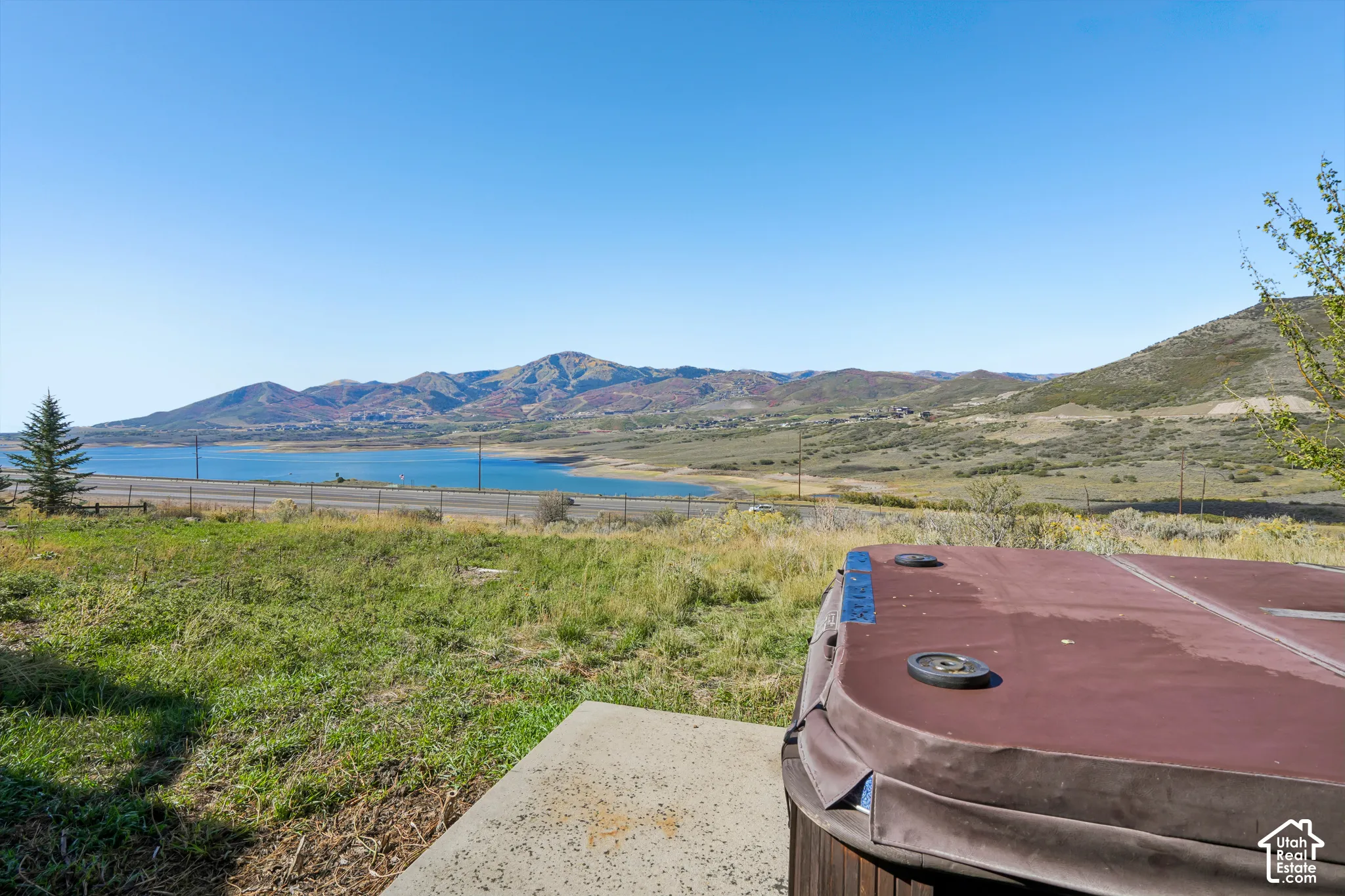 Patio area with a hot tub, surrounded by natural landscaping, offering a prominent water body and mountain backdrop