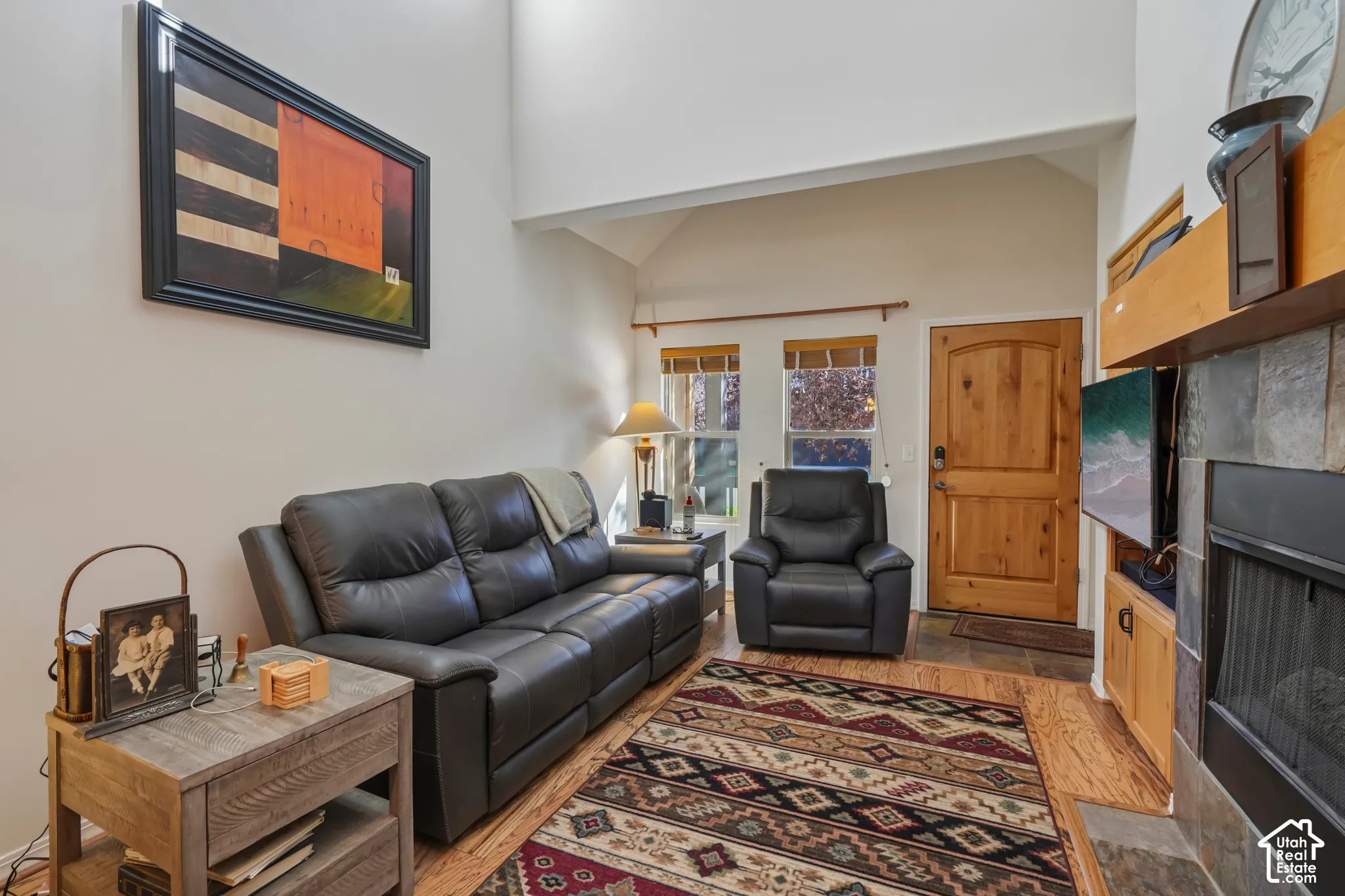 Vaulted ceiling, natural wood flooring, wood entry door, stacked stone fireplace, and built-in wood shelving