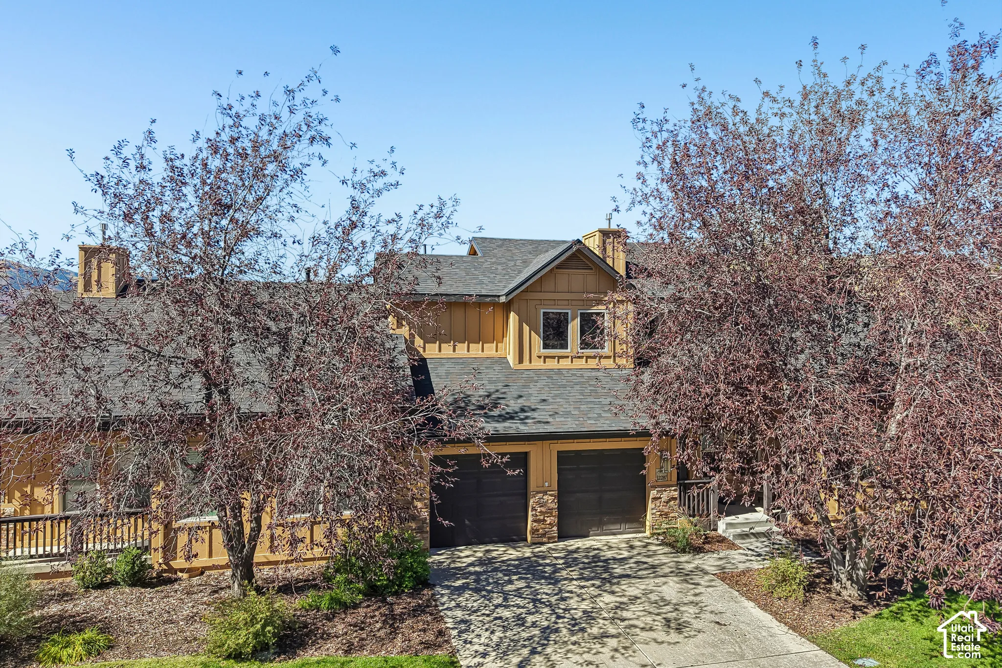 Craftsman-style exterior with wood siding, a dark shingle roof, two-car garage, stone accents, and an upper-level balcony with wood railing