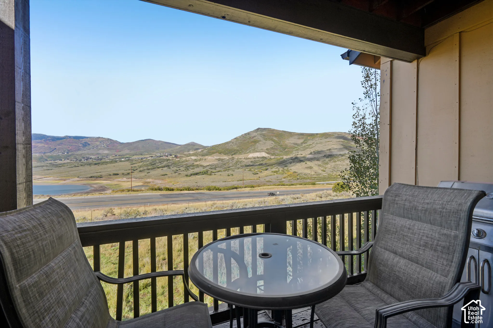 Covered balcony with a dark wood-finish railing, overlooking a scenic distant lake and mountainous terrain