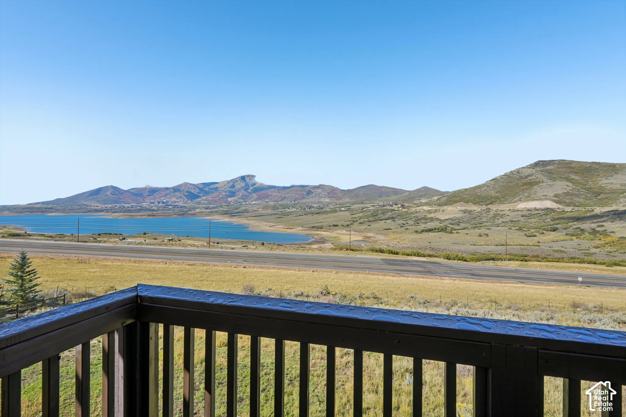 Outdoor deck with dark wood railing, overlooking a lake, mountains, and open terrain