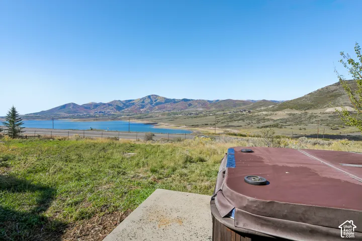 Patio area with a hot tub, surrounded by natural landscaping, offering a prominent water body and mountain backdrop