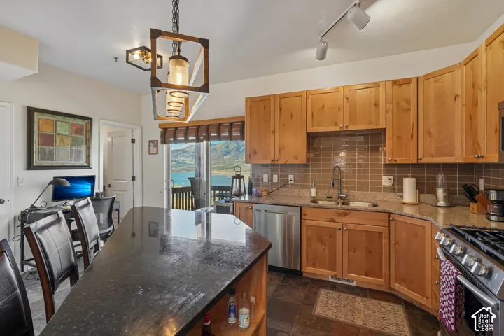 Kitchen featuring wood cabinets, stainless steel appliances, dark stone countertops, tile backsplash, and dark tile flooring