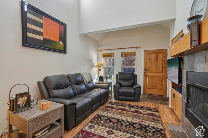 Vaulted ceiling, natural wood flooring, wood entry door, stacked stone fireplace, and built-in wood shelving