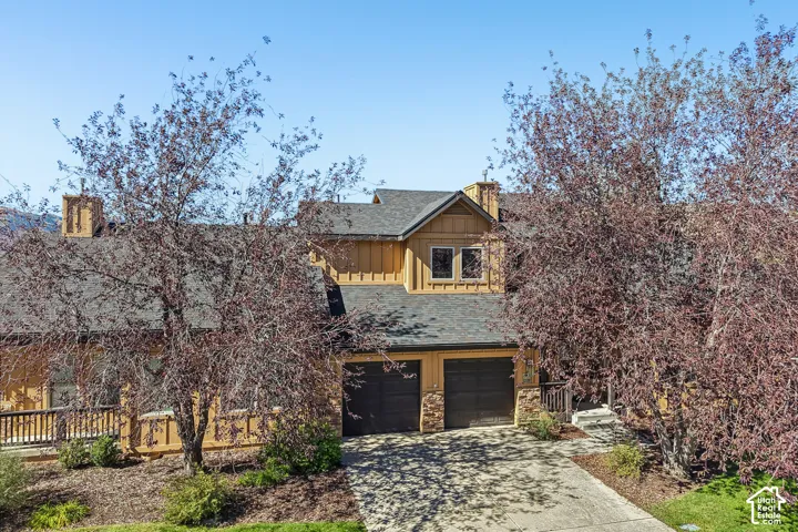 Craftsman-style exterior with wood siding, a dark shingle roof, two-car garage, stone accents, and an upper-level balcony with wood railing