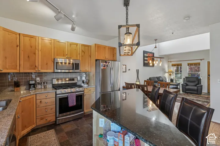 Kitchen with wood-finish cabinetry, stainless steel appliances, granite countertops, and tile backsplash