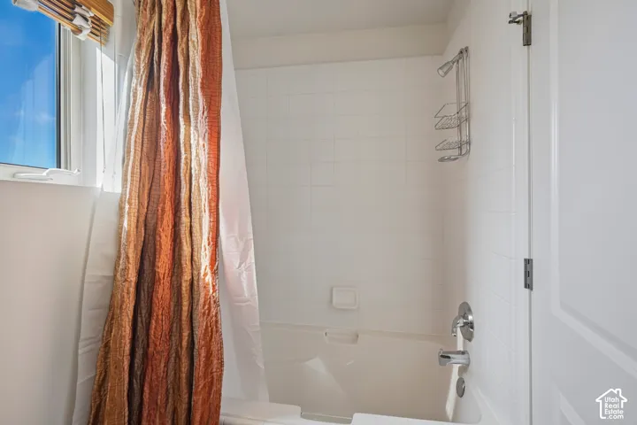 White tiled shower enclosure with a built-in tub, chrome fixtures, and an integrated window