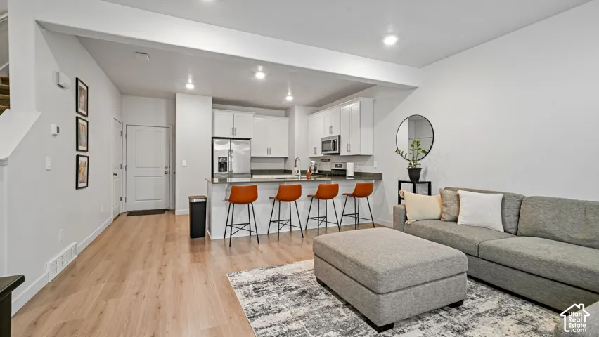 Open-concept living space with light-tone wood-finish flooring, recessed lighting, and a kitchen island with a dark countertop
