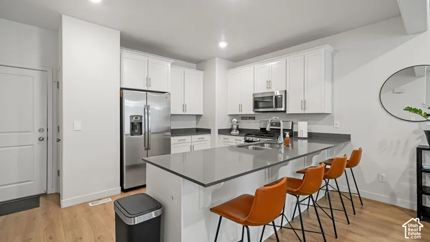 Modern kitchen featuring light wood-finish flooring, white cabinetry, dark countertops, and stainless steel appliances