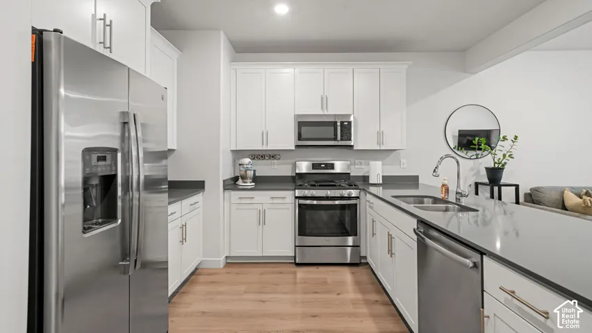 Kitchen featuring wood-finish flooring, white cabinetry, dark countertops, and stainless steel appliances including a refrigerator, dishwasher, and range