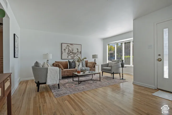 Spacious room featuring light wood flooring, a bay window, and a white entry door with vertical glass panels