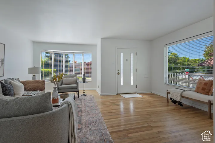 Spacious room featuring light wood flooring, a bay window, a large rectangular window, and a white entry door with vertical glass panels