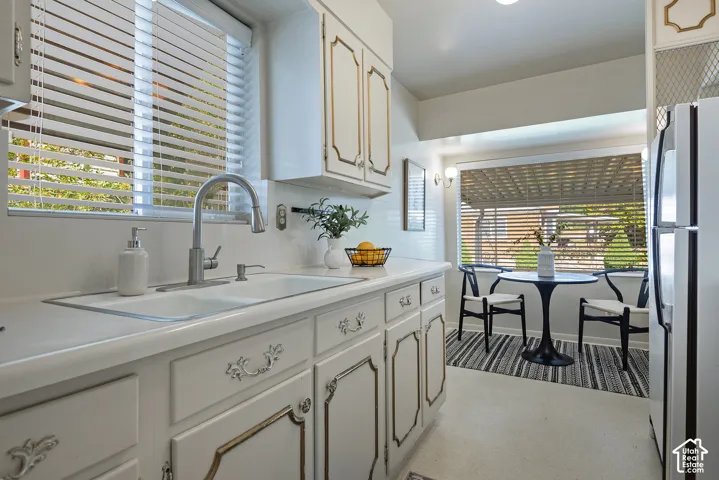 White cabinetry with decorative trim, dual-basin sink with a gooseneck faucet, light-colored countertops, recessed lighting, and a dining area with a large window