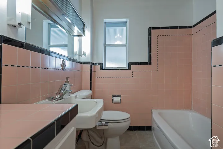 Bathroom featuring pink tiled walls with black trim, a porcelain sink with chrome fixtures, a built-in bathtub, and a window for natural light