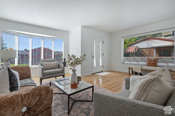Bright living area featuring wood flooring, a prominent bay window, and a white entry door