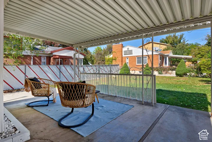 Covered concrete patio with white metal support posts, metal railing, and a manicured lawn