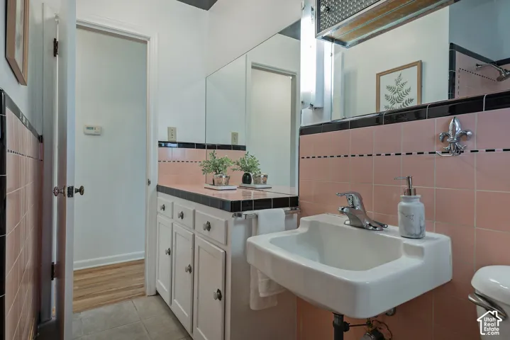 Wall-mounted sink with chrome fixtures, pink tile wainscoting, white cabinetry with black countertop, and a large wall mirror