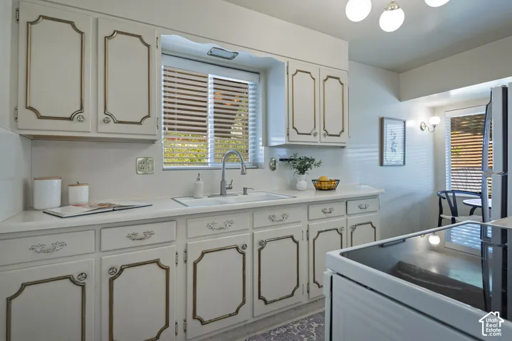 White cabinetry, dual basin sink with a gooseneck faucet, light-toned countertops, and a window with horizontal blinds