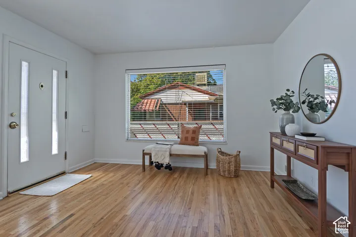 Hardwood flooring throughout, white painted walls, a white entry door with vertical glass inserts, and a rectangular window with horizontal blinds