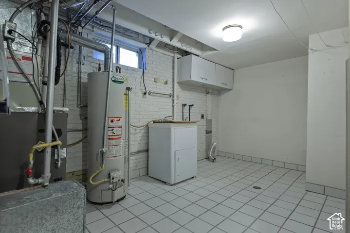 Tiled flooring, utility sink with base cabinet, upper wall-mounted cabinets, and a flush-mount ceiling light