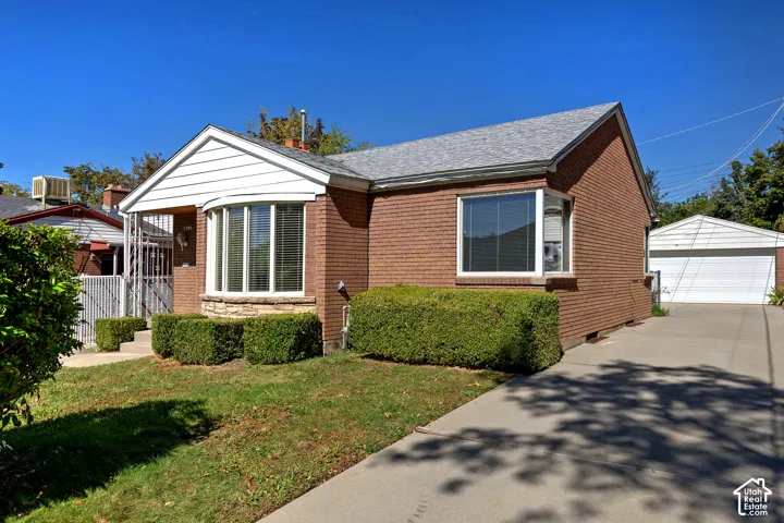 Brick exterior with white trim, a bay window, a concrete driveway, a detached garage, and mature landscaping