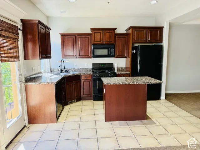 Kitchen featuring wood cabinetry, dark-finish appliances, light-toned tile flooring, and stone-look countertops