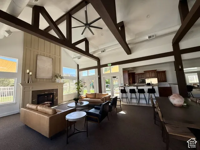 Vaulted ceilings with exposed wood beams, a stone-surround fireplace, large windows, French patio doors, and a built-in kitchen bar