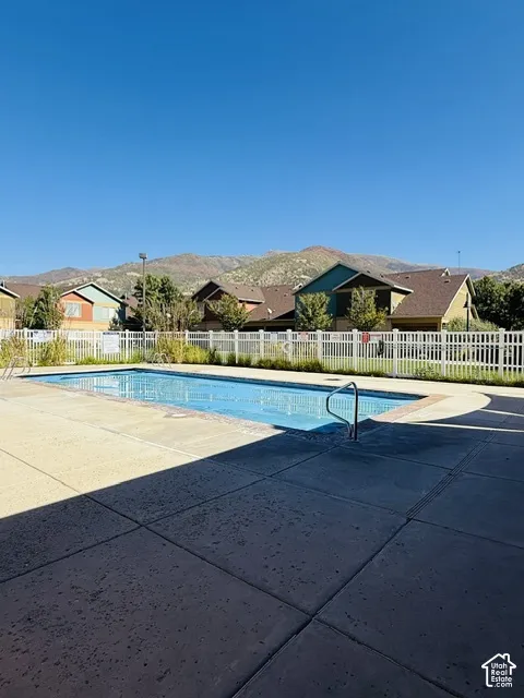 Swimming pool with concrete decking, a white picket fence, and distant mountain scenery