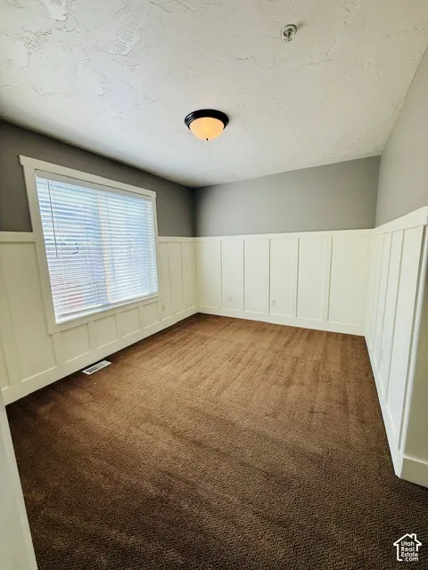 Brown carpeted flooring, white wainscoting, and a single window with blinds