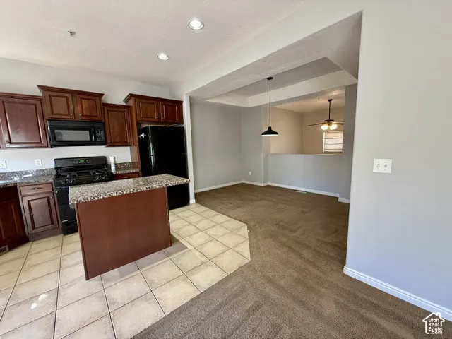 Kitchen featuring dark wood-finish cabinetry, black appliances, and a central island with a granite-style countertop