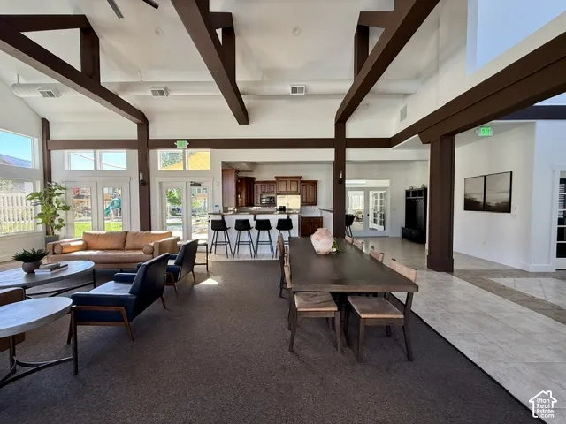 Vaulted ceilings with exposed beams, expansive windows, built-in kitchen cabinetry, and French doors leading to an outdoor space