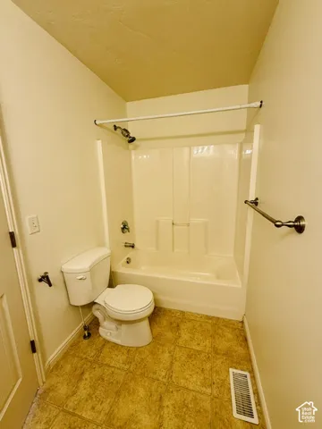 Bathtub/shower combination with a single-handle faucet, white toilet, and patterned flooring