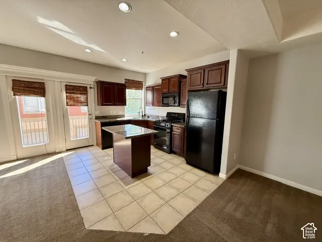 Kitchen featuring dark wood cabinetry, a central island with a stone countertop, and black appliances
