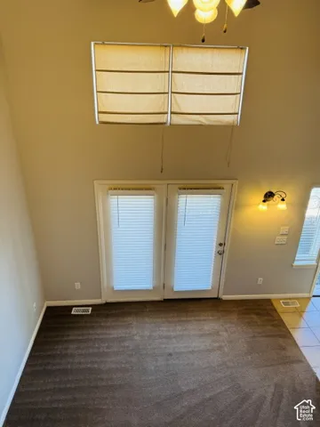 High ceilings with a ceiling fan, dual upper windows with shades, double glass doors with blinds, wall sconce lighting, and carpet flooring