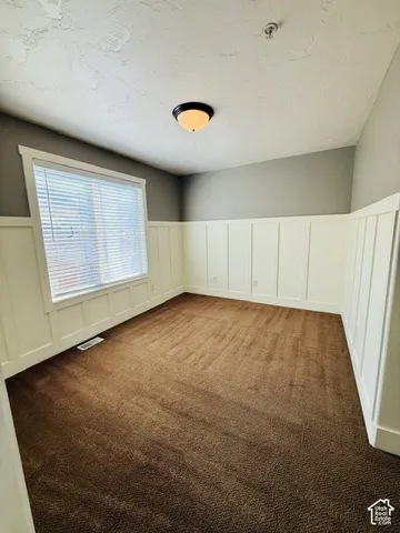 Brown carpeted flooring, white wainscoting, and a single window with blinds