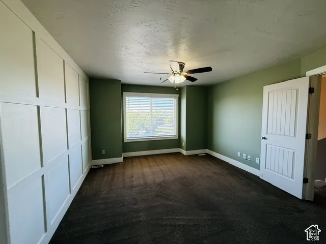 Board and batten accent wall, ceiling fan with light fixture, large window with blinds, dark carpet flooring, and a paneled door